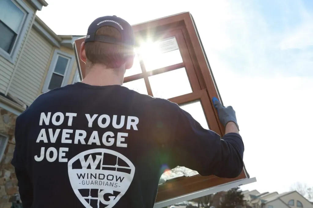 Window Guardians installer carrying a brown replacement window frame in sunlight