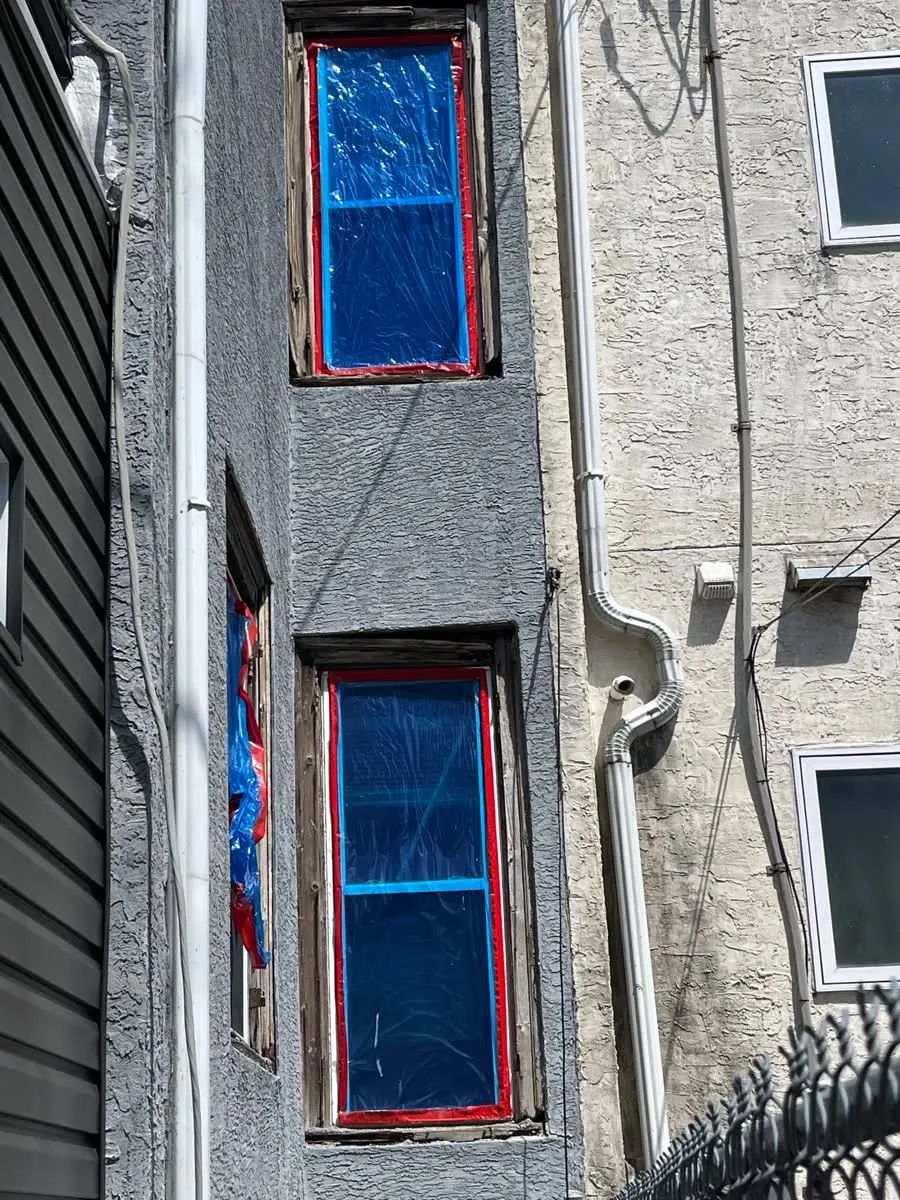 Rowhome windows covered in plastic sheeting with damaged frames