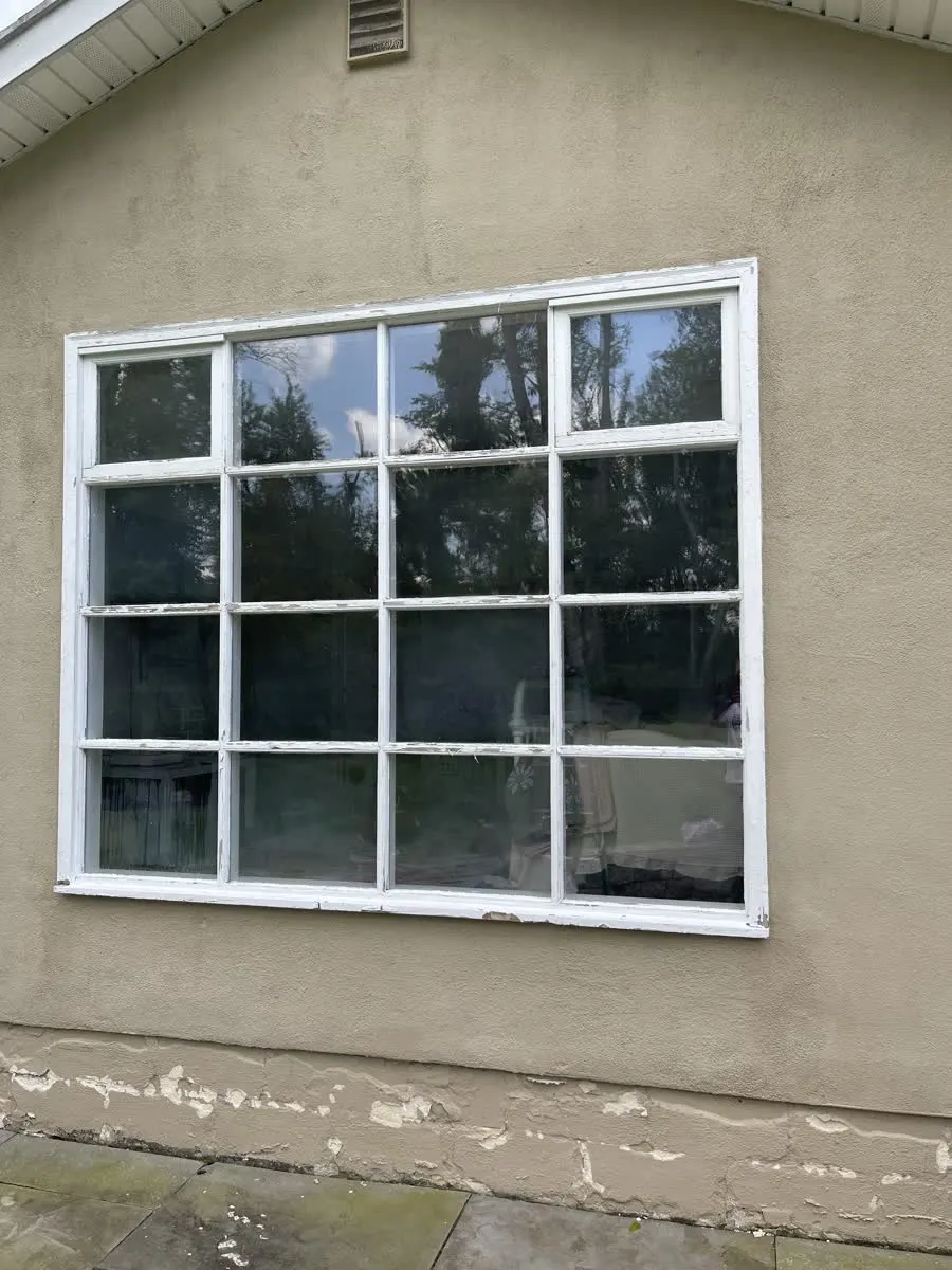 Old sixteen-pane window with peeling paint on a stucco wall