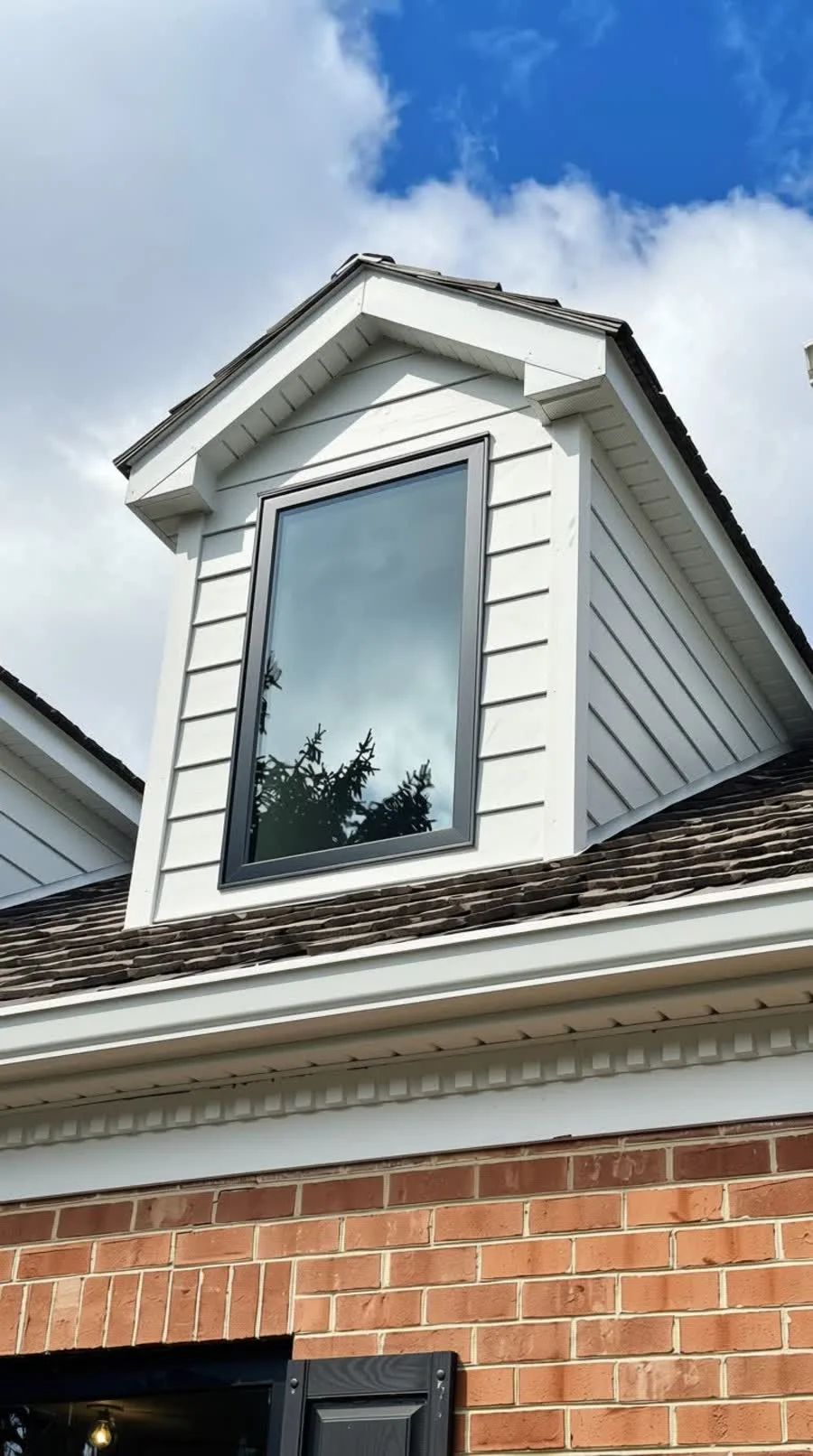 Black-framed dormer window in white siding above a brick wall