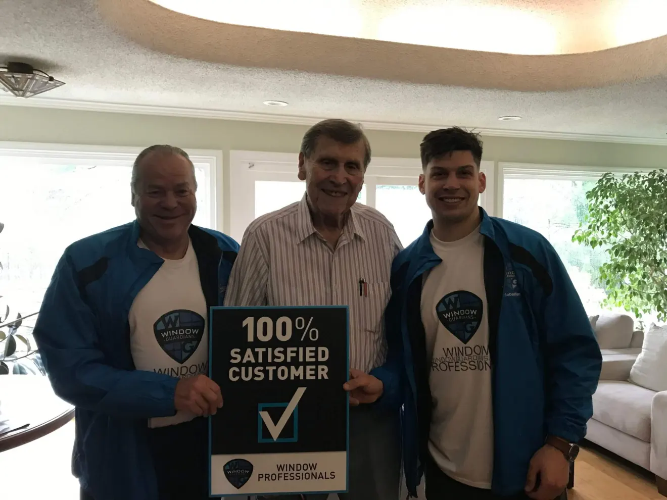 Window Guardians customer holding a 100 percent satisfied customer sign with the installation team